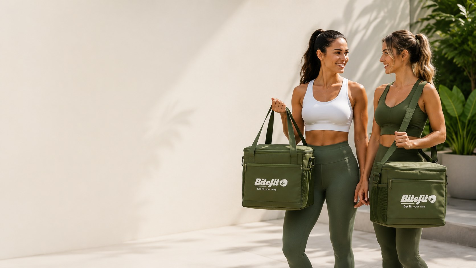 Two women in gym wear carrying Bite Fit cooler bags in the sunshine